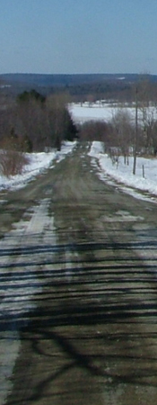 dirt road trailing off into sky through snowy farm land